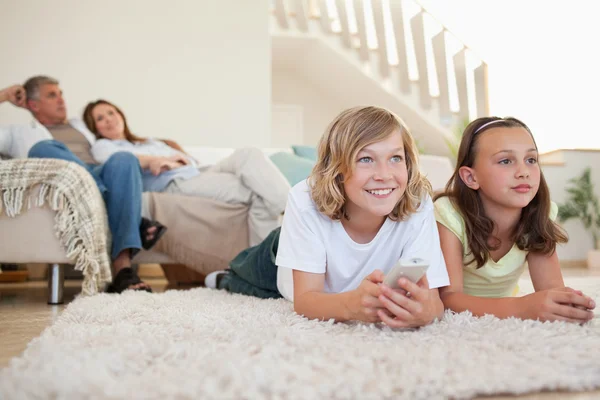 Братья и сестры лежат на ковре и смотрят телевизор. — стоковое фото