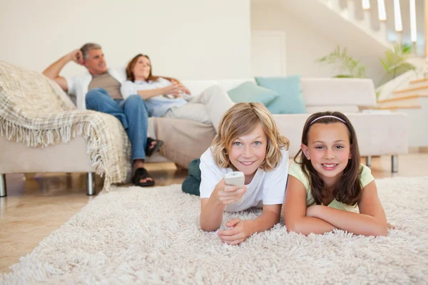 Hermanos acostados en la alfombra viendo la televisión —  Fotos de Stock