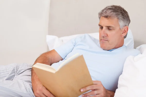 Зрелый мужчина читает книгу в постели — стоковое фото