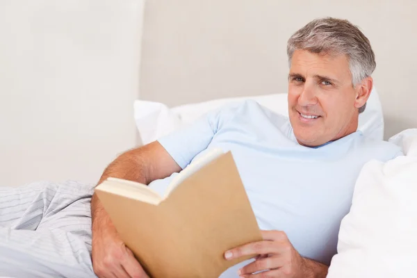Glimlachende man met boek in bed — Stockfoto