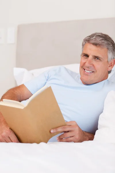 Lächelnder Mann beim Lesen im Bett — Stockfoto