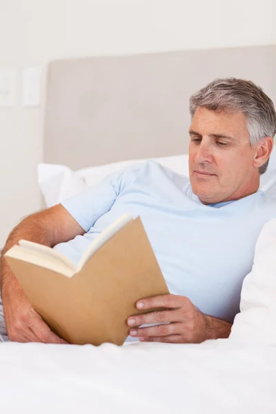 Man reading book in bed — Stock Photo, Image