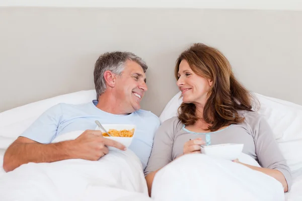 Casal feliz comer cereais na cama — Fotografia de Stock