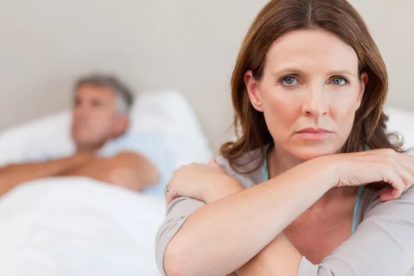 Sad woman on the bed with husband in background — Stock Photo, Image