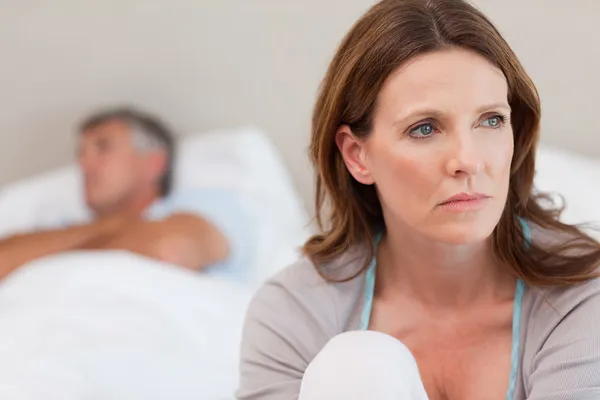 Sad woman on bed with her husband in the background — Stock Photo, Image