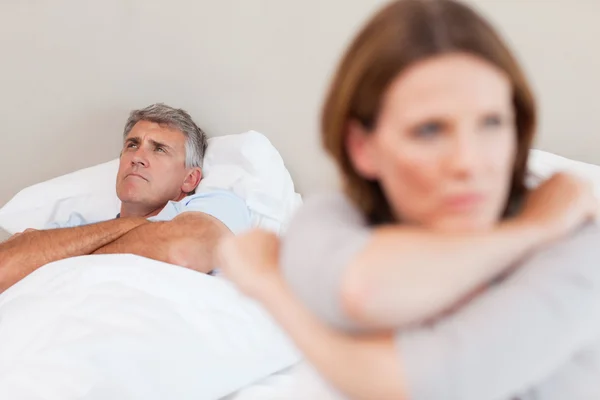 Ledsen man i säng med sin hustru i förgrunden — Stockfoto