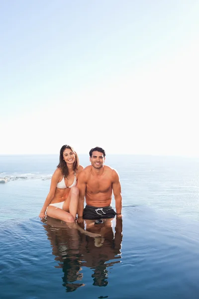 Paar sitzt auf Poolrand mit Meer im Hintergrund — Stockfoto
