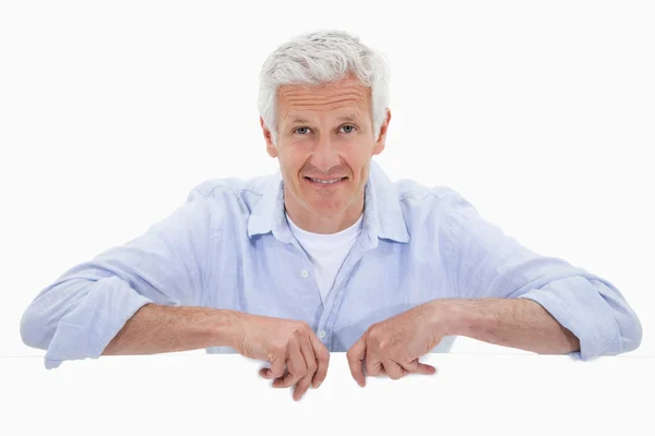 Portrait of a smiling mature man standing behind blank panel — Stock Photo, Image