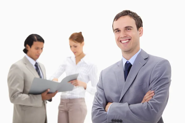Smiling young businessman with talking colleagues behind him — Stock Photo, Image