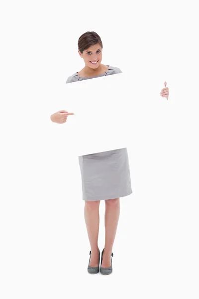 Smiling woman pointing at blank sign in her hands — Stockfoto