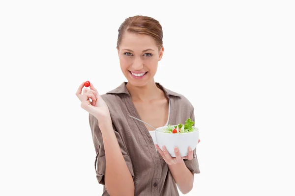 Женщина с миской салата и маленьким помидором в пальцах — стоковое фото