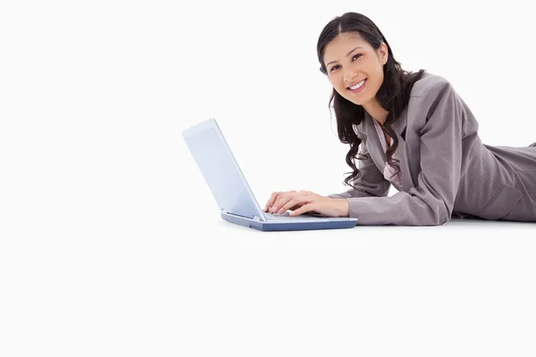 Vista laterale della donna sorridente sdraiata mentre lavora sul computer portatile — Foto Stock