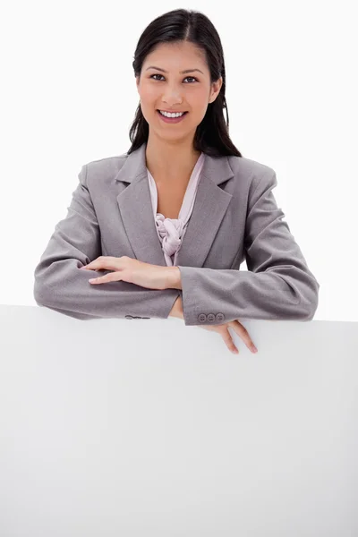 Smiling young businesswoman leaning on blank wall — Stock Photo, Image