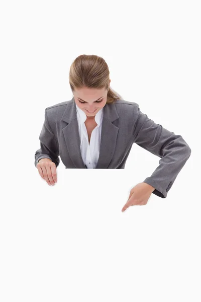 Bank employee pointing down at blank sign in her hands — Stock Photo, Image