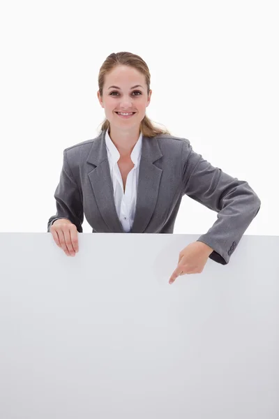 Smiling bank employee pointing down at blank sign — Stock Photo, Image