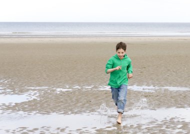 The boy in a green hoodie, running barefoot on the beach at low clipart