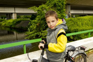 Young cute school boy with bicycle on the bridge clipart