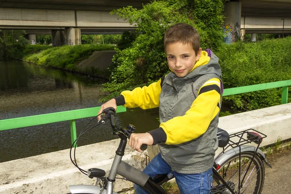 Ung söt leende skolan pojke med cykel på bron — Stockfoto