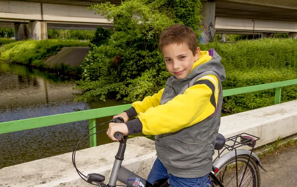 Ung söt leende skolan pojke med cykel på bron — Stockfoto
