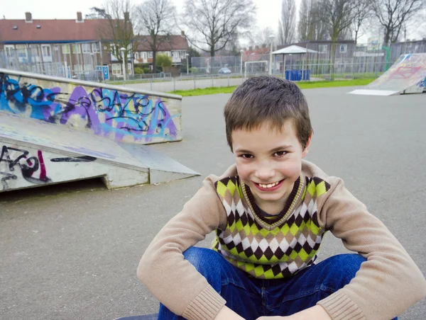 Симпатичный улыбающийся мальчик, сидящий на детской площадке — стоковое фото