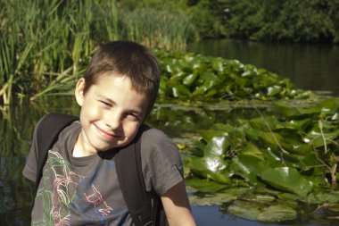 Smiling boy sitting at lake in summer clipart