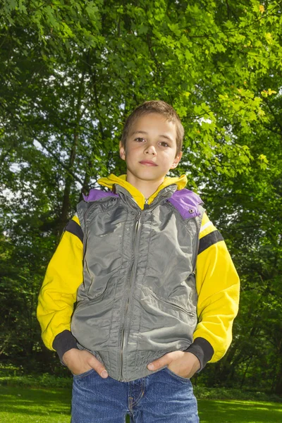 Niño lindo en una sudadera con capucha amarilla contra los árboles verdes fondo —  Fotos de Stock