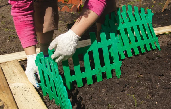 :Женщина устанавливает зеленый пластиковый забор на клумбе — стоковое фото