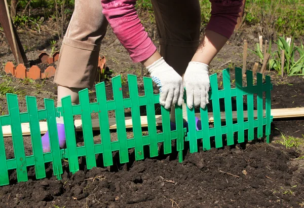 :the woman establishes a green plastic fencing on a flower bed — Stock Photo, Image