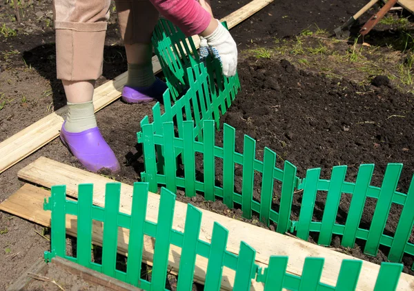 :die Frau errichtet einen grünen Plastikzaun auf einem Blumenbeet — Stockfoto