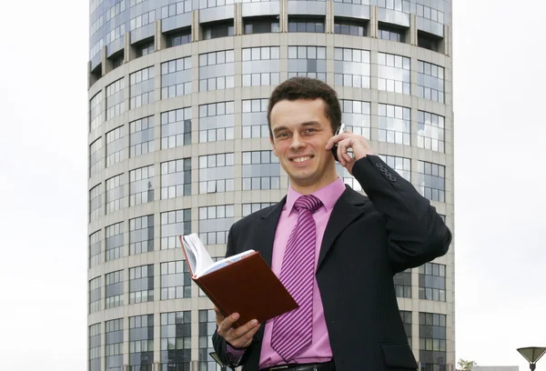 Attraktiv ung affärsman använder en mobiltelefon framför en modern kontorsbyggnad — Stockfoto