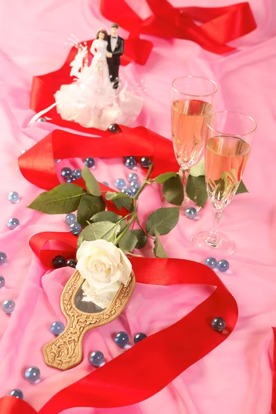A photo of wedding cake dolls, rose and glasses over pink — Stock Photo, Image