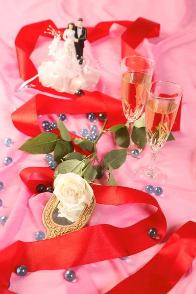 A photo of wedding cake dolls, rose and glasses over pink — Stock Photo, Image