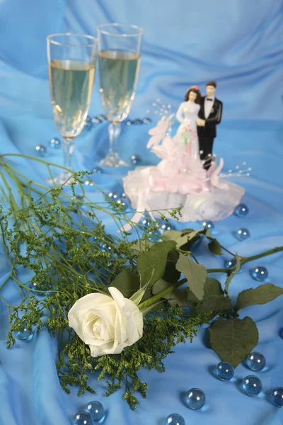 A photo of wedding cake dolls, rose and glasses over blue — Stock Photo, Image