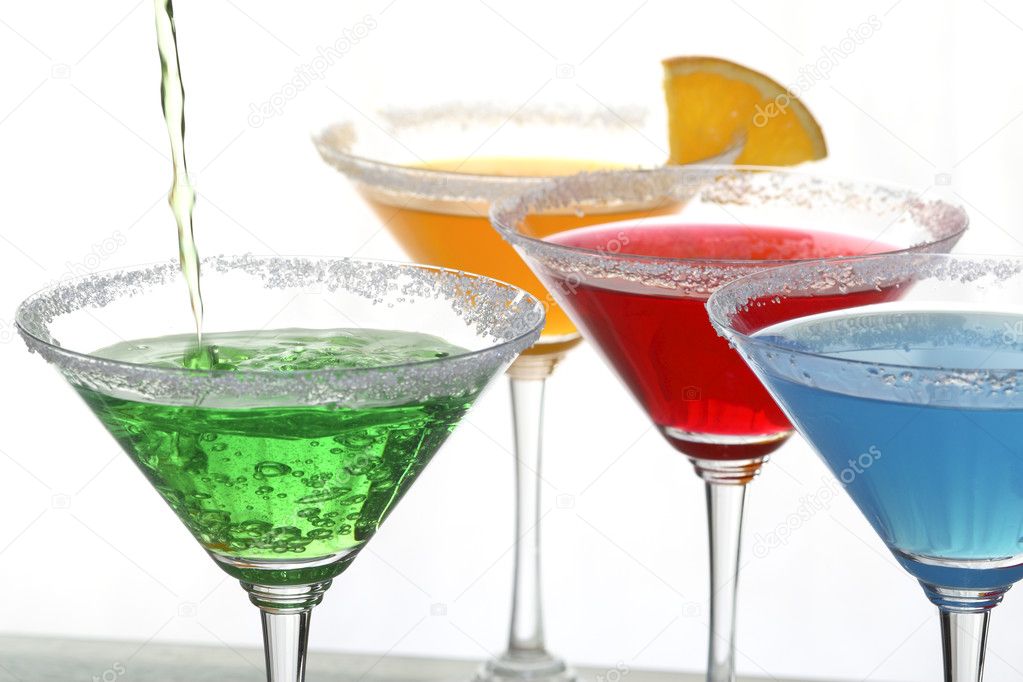 A close up view of martini glass with different colored cocktails and a piece of orange