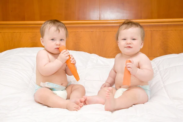 A két szép meztelen pufók baby ikrek és étkezési sárgarépa — Stock Fotó