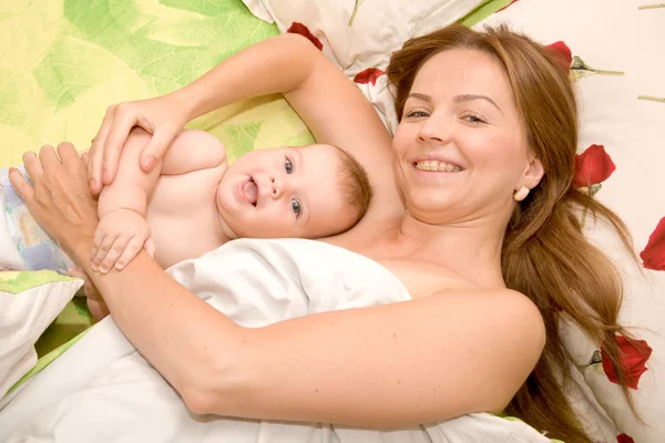 Мама с улыбающимся ребенком лежит в постели — стоковое фото