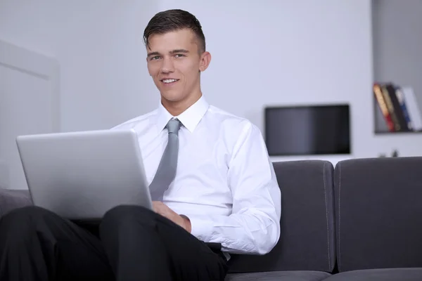 Glad ung affärsman tittar och ler oss, sitter på soffan — Stockfoto