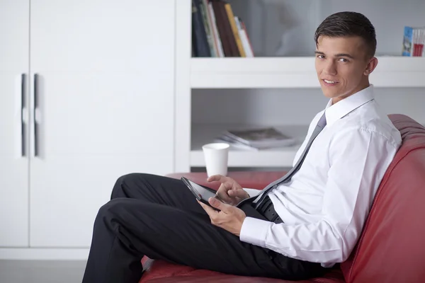 Feliz joven hombre de negocios con la tableta en el sofá en la oficina sentado —  Fotos de Stock