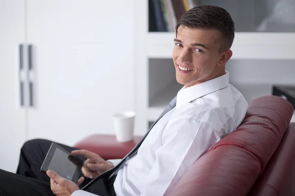 オフィスのソファでタブレットを保持している青年実業家の笑みを浮かべてください。 — ストック写真