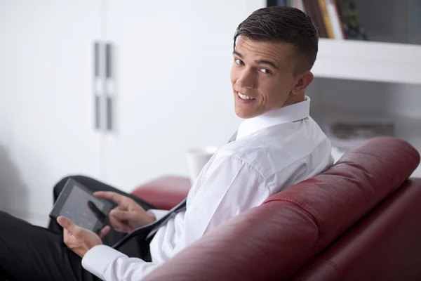 Szczęśliwy młody biznesmen z tabletek na kanapie w biurze siedzi — Zdjęcie stockowe