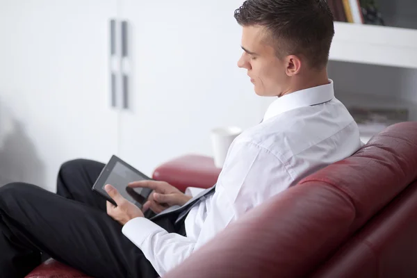 Mosolygó fiatal üzletember, fogta a tabletta a hivatalban kanapé — Stock Fotó