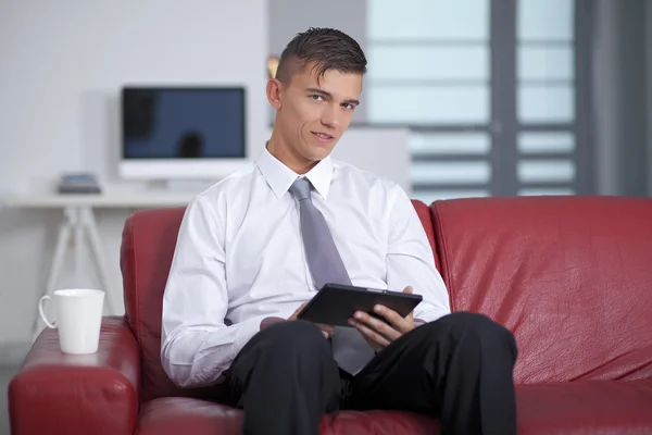 Jeune homme d'affaires souriant tenant une tablette sur le canapé au bureau — Photo
