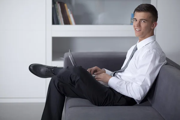 Χαμογελώντας επιχειρηματίας που εργάζεται με ένα σημειωματάριο και να κάθεται στον καναπέ — Φωτογραφία Αρχείου