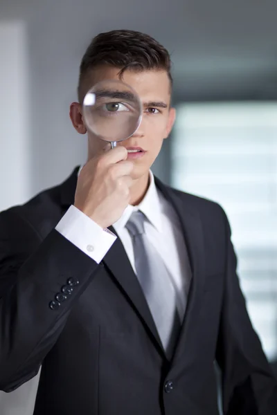Jovem homem de negócios em um terno olhando através de uma lupa — Fotografia de Stock