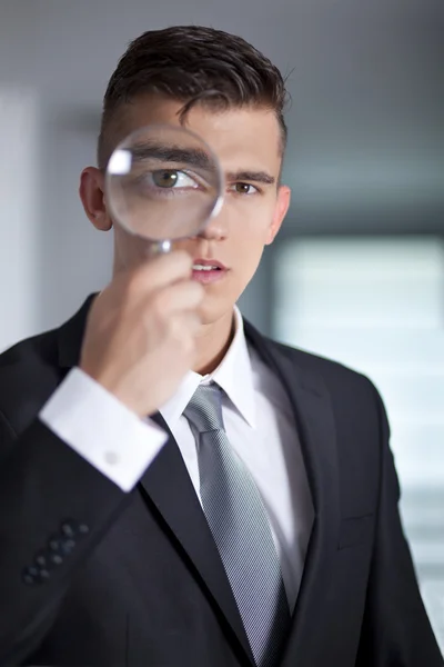 Молодой бизнесмен в костюме смотрит в увеличительное стекло — стоковое фото