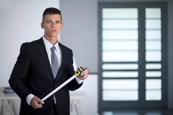 Joven hombre de negocios en un traje con una cinta métrica y mirando — Foto de Stock