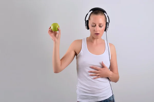 Ελκυστική Μπλόντι γυναίκα, κρατώντας ένα μήλο και να ακούτε μουσική — Φωτογραφία Αρχείου
