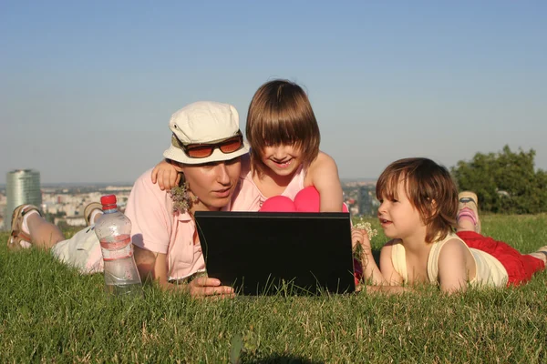Mother and daughters at work on the notebook in park — Stock Photo, Image