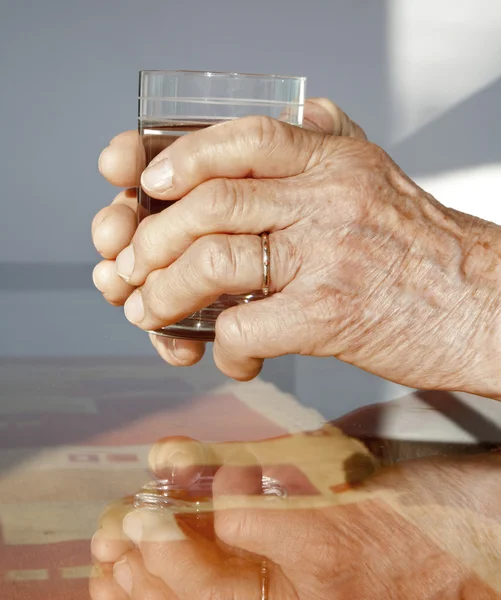 Hände einer alten Frau und ein Glas Wasser — Stockfoto