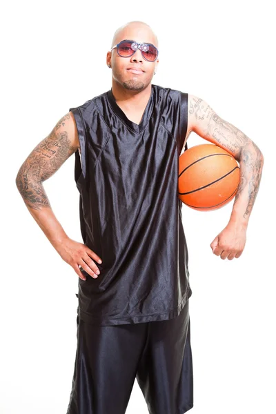 Studio porträtt av basketspelare som bär svarta solglasögon ständiga och hålla bollen isolerade på vitt. tatueringar på armarna. — Stockfoto